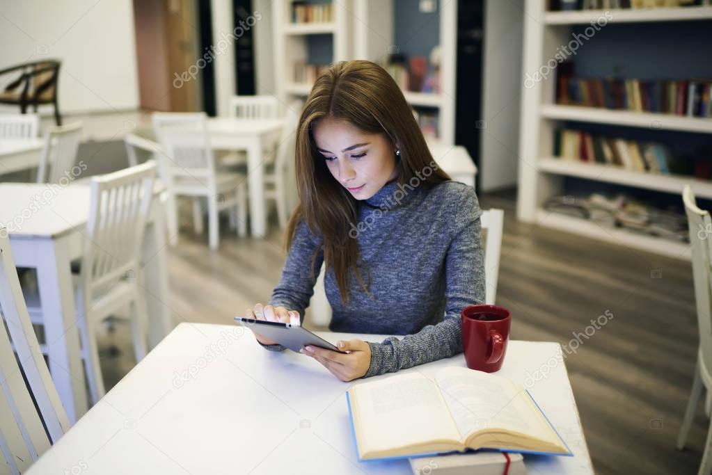 Concentrated girl via digital device connected to fast 5G wireless in university library wifi zone