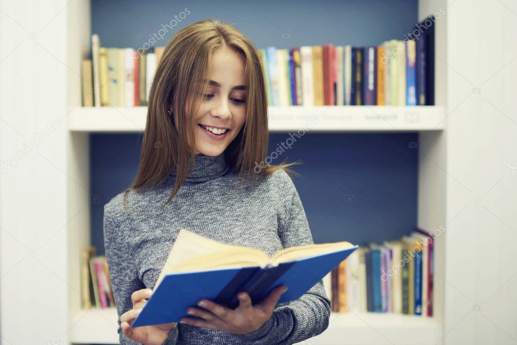 Young attractive female student thinking over plot of detective story while reading book 