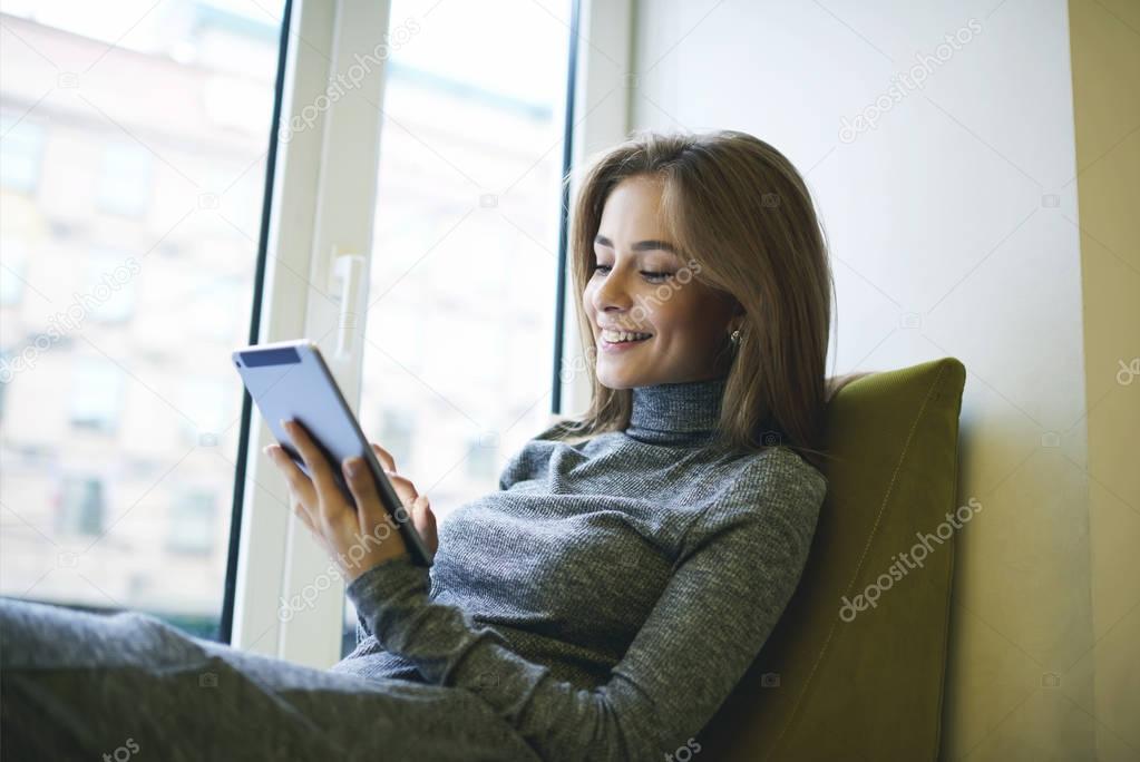 Portrait of young attractive female relaxing after hard working day sitting near lighting window in cozy chair 