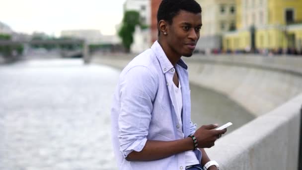 Темнокожий турист, стоящий на улице со смартфоном — стоковое видео