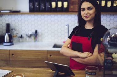 Profesyonel kadın barista modern cihazların yakınında duran istemci için aroma kahve yapmak için sipariş bekliyor