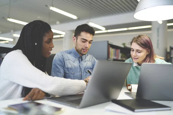 Grupo multirracial de estudantes internacionais colaborando no projeto em biblioteca universitária — Fotografia de Stock