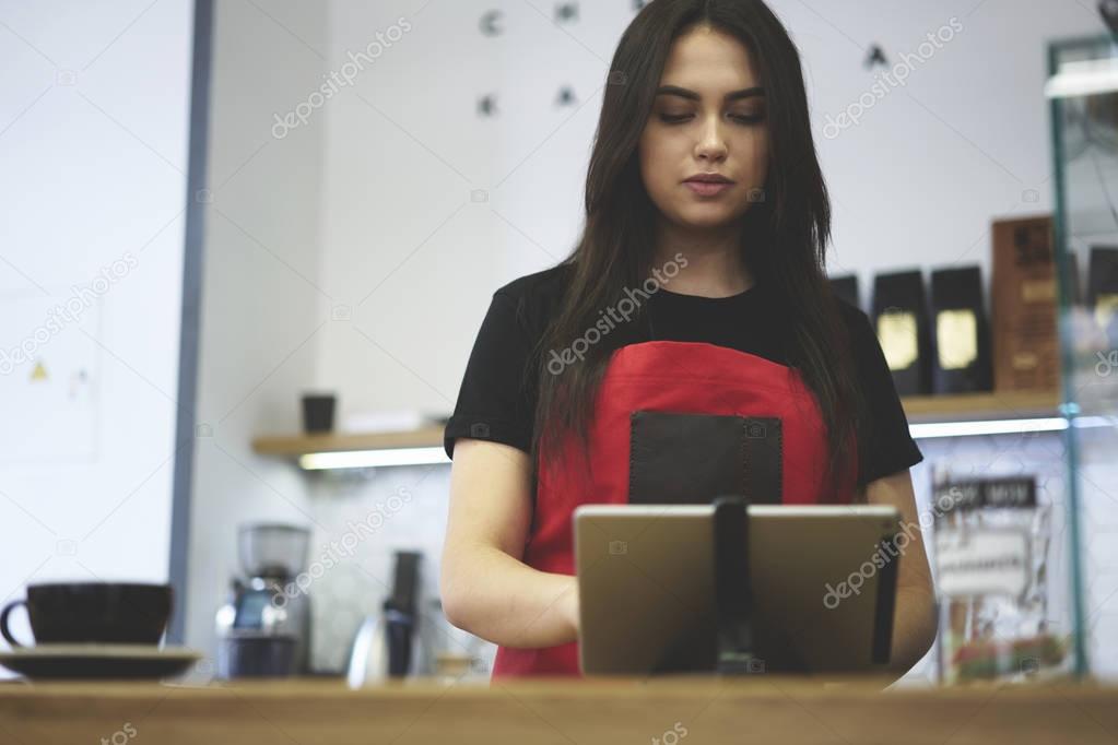 Charming serious waitress using application for checking finance information of incomes