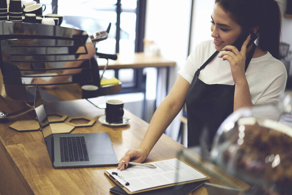 Female coffee shop owner standing near coffee machine at bar with modern laptop
