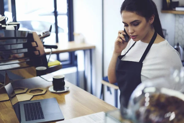 Mujer joven empleada de cafetería hablando con el jefe en el celular y reportándolo sobre los ingresos de la jornada laboral — Foto de Stock