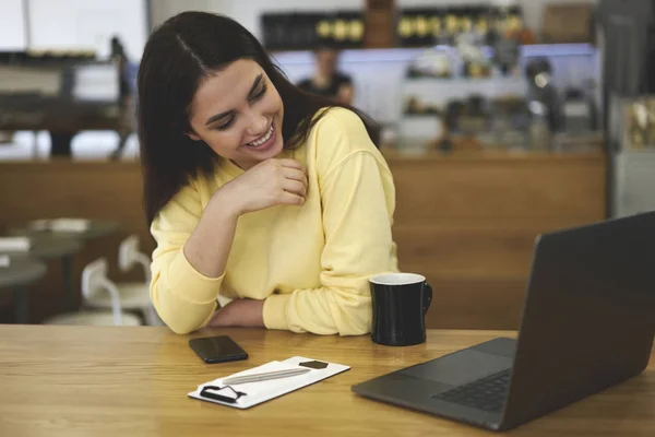Smiling female freelancer sitting in designer cafeteria interior enjoying cup of aroma coffee — Stock Photo, Image