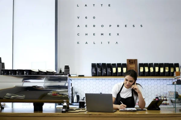 Garçonetes femininas sentadas no bar com laptop enquanto conversam com administrativo no smartphone Fotos De Bancos De Imagens