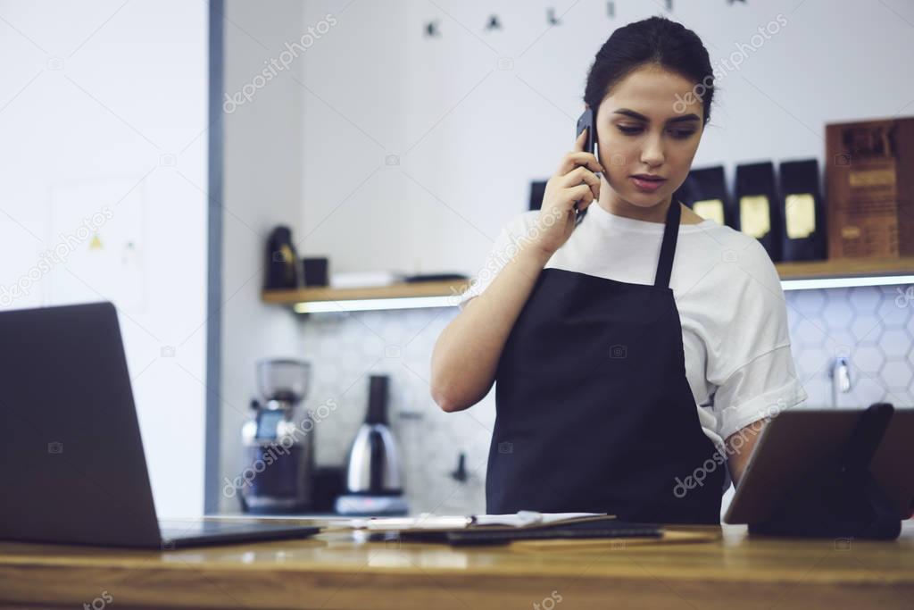 Woman coffee shop owner making finance accounting standing at bar with modern laptop and digital tablet