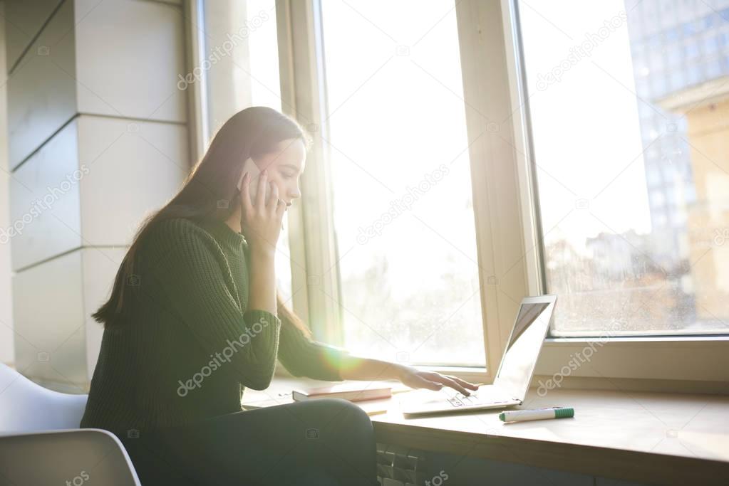 Young businesswoman talk on phone while installing browser application on modern laptop.