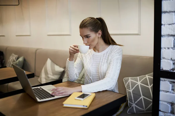 Charmante blogger bezig met het schrijven van nieuwe verhalen op laptop en binnenshuis smakelijke koffie drinken — Stockfoto