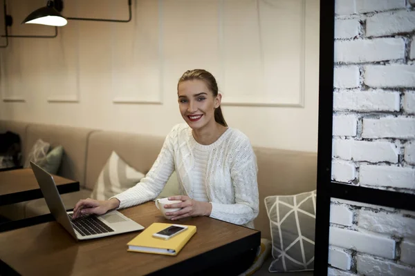 Mujer freelancer utilizando internet gratis en la cafetería y mirando a la cámara con buen humor —  Fotos de Stock