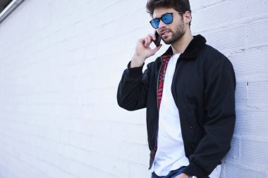 Trendy kıyafetler ve şık güneş gözlüğü için cep üzerinden en iyi arkadaşı aradım giymiş yakışıklı beyaz modeli.