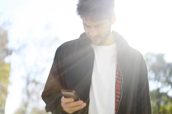 Young bearded hipster guy casual dressed in style look walking outdoors in city using online application on cellphone. — Stock Photo, Image