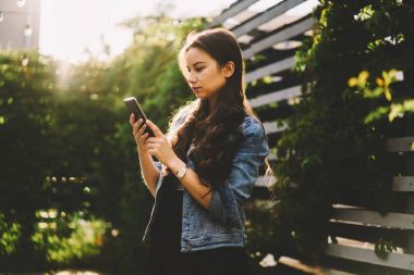 Smartphone aygıt açık havada kentsel ortamda ayakta yeni mobil uygulama yükleme güzel esmer genç kadın. Hippi kız telefonu alınan sms mesajý okuma denim ceket giymiş