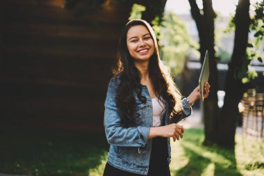 Güzel esmer saçlı modern tablet elinde tutan ve yüzünde gülümseme ile kameraya bakarak mutlu genç kadın yarım uzunluk portre. Dijital dokunmatik ped açık havada duran ile neşeli erkek