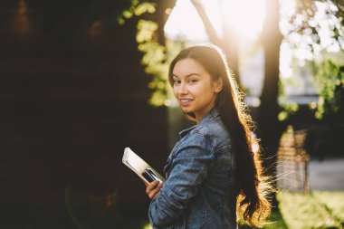 Kameraya bakarak elinde yarım uzunluk portre çekici gülümseyen hipster kızla kitaplar. Neşeli öğrenci not defteri açık havada süre ayakta tutan Kot ceket giymiş. Kopyalama alanı alanı