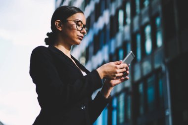 İcra müdürü 4 g kullanarak finansal haber okuma zarif siyah takım elbise giymiş gözlük yan görünüm office promosyon arka plan üzerinde dururken smartphone Internet bağlı