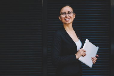 Başarılı işkadını yarım uzunluk portre fotoğraf makinesi ayakta mali bilgilerinizi için tanıtım alanının yakınında gülüp modern tablet aygıtı elinde tutan şık giyim giyinmiş