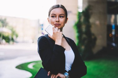 Holding modern cep telefonu ve klasör el süre uzağa arıyorsunuz ve sokak promosyon arka plan üzerinde duran iş fikirleri üzerinde düşünme şık siyah elbiseli düşünceli kadın icra müdürü