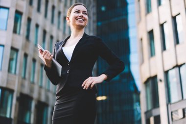 Müreffeh neşeli profesyonel Yöneticisi dijital tablet cihaz tutan ve uzak ofis binası yakınındaki açık havada duran seyir siyah formal giyim giymiş. Touch pad gadget ile başarılı bankacı