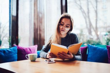 Optik Gözlük tahta masada oturan boş zaman içinde ilginç bir kitap okuma dalgın zeki öğrenci.