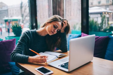 Yorgun öğrenci notları ders kitabı sırasında bilgisayar kullanarak coworking de ödevini yapma.