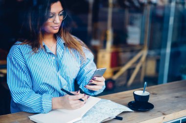 Genç kadın tasarımcı uzaktan kahve dükkanında çalışarak ve modern telefon aygıtı üzerinde online ödeme yapma.