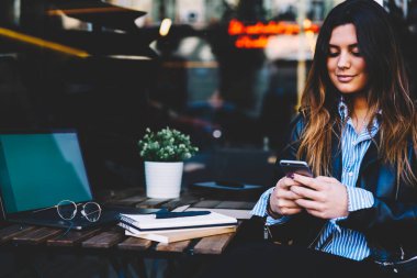 Dizüstü bilgisayar başında otururken modern smartphone cep telefonu ile sosyal ağlarda arkadaşlarınızla çevrimiçi sohbet mesajlaşma şık genç kadın serbest meslek.