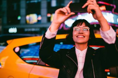 Akşam boş vaktinizi, çekici kadın blogger resim ayakta kentsel akşam konuşmak için poz selfie yapma gece aydınlatma yansıması ile hippi kız gözlük gülümseyen 