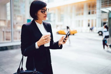 Genç kadın yöneticisi olarak şık giysiler bloglama ağlar ile cep telefonuna mesaj gönderme gözlük git, kendine güvenen işkadını kahve molası dururken internet kullanımı