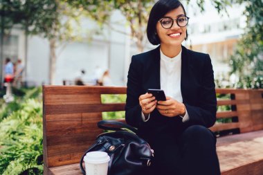 Kahve bankta oturan ve smartphone tarafından ileti gönderme arası harcama şirketinin müreffeh sahibi portresi.