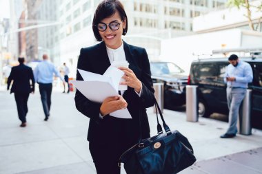 Açık havada ve trendy çanta gitmek dururken kahve ile belgelerin incelenmesi kadın sahibi gülümseyen, zarif yapılan başarılı işkadını giymek bir sürü paket cu ofiste aceleyle görevleri yapma