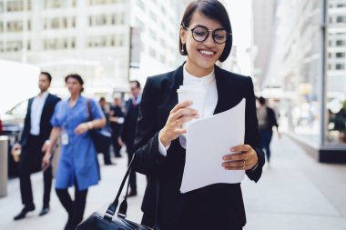 Gitmek için meşgul kadın yönetici Yöneticisi'nde kahve ile sokakta yürürken belgelerin incelenmesi gözlük.