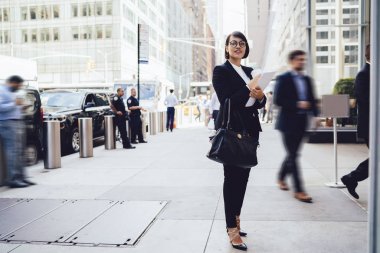 İşkadını resmi kıyafeti ayakta belge ve çanta ile kalabalık Caddesi üzerinde tam uzunlukta.