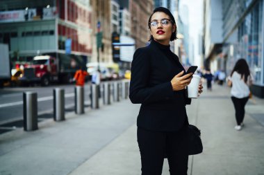 Trendily kadın Yöneticisi smartphone posta iletileri gönderme gitmek için manhattan sokak, güzel işkadını kırmızı dudaklı ve kahve ile yürüyüş gözlük üzerinde gezinme sırasında kontrol holding giyinmiş