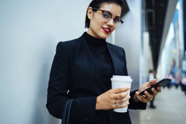 Kendine güvenen işkadını zarif kıyafetiyle kamera kahve ile smartphone cep telefonu ile mesaj göndermek bakarak gitmek portresi.