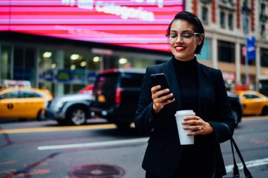 Başarılı kadın yönetici trendy Eyewear kahve ile cadde üzerinde taksi beklerken sohbet online gitmek.