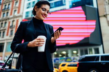 Gitmek için taksi ayakta kahve ile Caddesi'nde beklerken cep telefonunuzda getting haber iyi haber ile kadın tüccar gülümseyen.