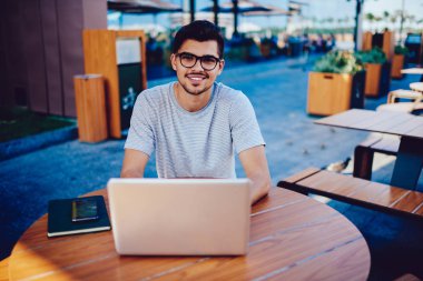 Modern dizüstü bilgisayarda yazılım güncelleme ve kameraya bakarak serbest çalışma gülümseyen erkek programcı portresi.