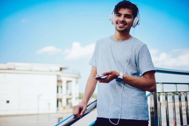 Neşeli hipster adam ayakta açık havada dinleme müzik modern cihaz kullanarak portresi.