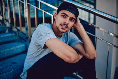 Genç hipster adam portresi merdivenlerde oturan trendy sokak kıyafeti giymiş.
