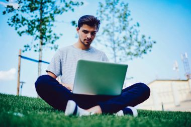 Genç erkek öğrenci dizüstü bilgisayarda online araştırma yapmaktan konsantre.