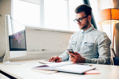 Konsantre genç bu geliştirici bilgisayarda office çalışırken posta smartphone cep telefonu ile kontrol.