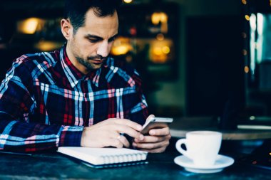 Genç adam fincan cappuccino Cafe cep telefonuyla görüntü kırpılmış.