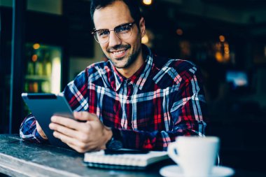 Gözlük uzaktan kameraya gülümseyen tablet üzerinde çalışma neşeli genç adam portresi yarım uzunluk.