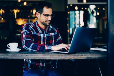 Genç adam metin yazarı şık gözlük kahvehane iç oturan modern dizüstü bilgisayardaki bilgilere klavye yoğunlaştı. Erkek grafik tasarımcı çalışma serbest dijital netbook