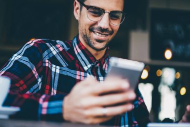 Şık Eyewear modern telefon aygıtı üzerinde ücretsiz Wi-Fi bağlantısını kullanarak internet sitelerinde komik video izlerken neşeli genç adam görüntü kırpılmış. Olumlu erkek cep üzerinde uygulama yükleme