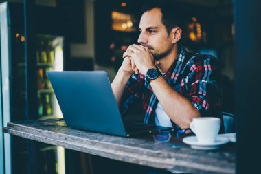 Dijital netbook aygıt oturma ve ücretsiz yüksek hızlı internet bağlantısı ile şık kafe iç modern grafik oluşturmak için yeni fikirler üzerinde düşünme düşünceli yakışıklı genç tasarımcısı