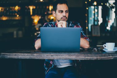 Modern dijital dizüstü bilgisayar başında oturan ve uzakta ile lezzetli kahve kafeteryasında oturan bakarken yeni proje üzerinde düşünme hipster adam durulması. Yeni başlangıç iş planlama düşünceli adam