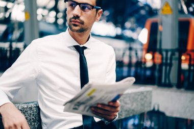 Trendy Eyewear uzakta popüler gazetesi elinde tutarken seyir durulması erkek uzman görüntüsünü kapatın. Dalgın işadamı ile kitle iletişim araçları-toplantı için bekleyen harcamak zaman kadeh kırpılmış
